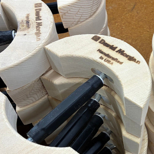 Close-up of stacked light wood carving or woodworking blocks with black-handled tools inserted, branded with 'David Morgan Handcrafted in USA' engraved on the wood.